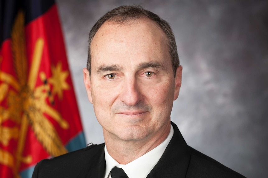 David Johnston, wearing his Navy uniform, sits in front of a grey background and Australian flag.