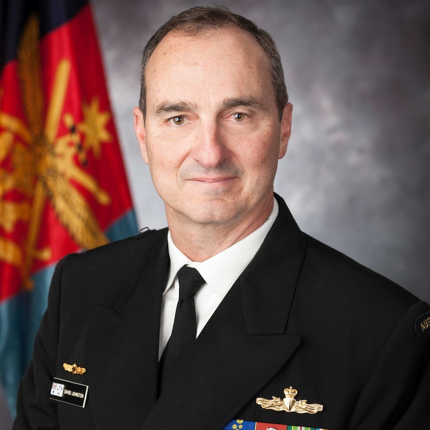 David Johnston, wearing his Navy uniform, sits in front of a grey background and Australian flag.