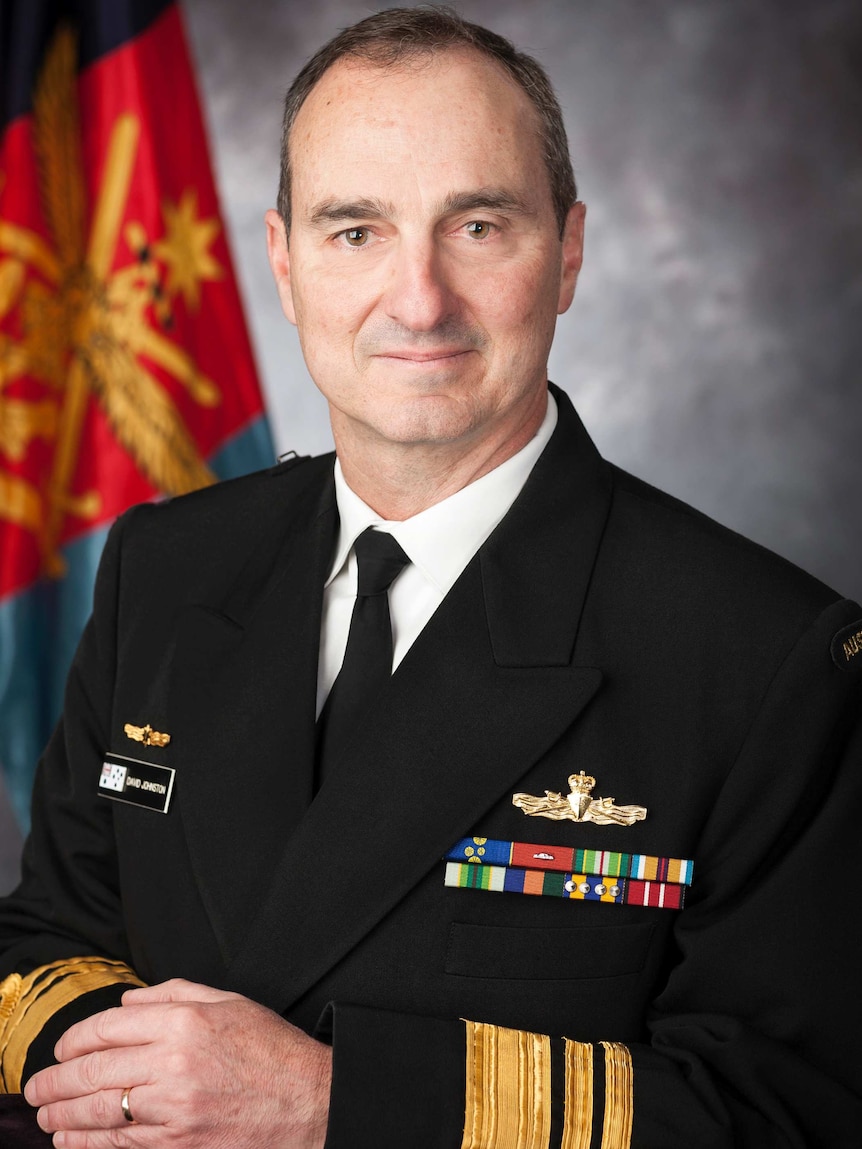 David Johnston, wearing his Navy uniform, sits in front of a grey background and Australian flag.