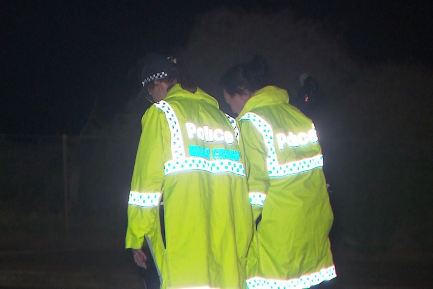 Two police officers wearing yellow hi-vis jackets in the dark