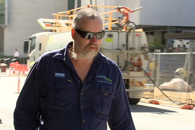 A mid shot of a man in a blue work top and sunglases walking down a Perth street outside the Supreme court.