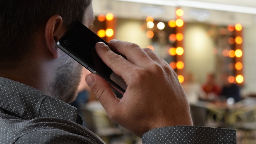 A man wearing a grey collared shirt holds a mobile phone to his ear.