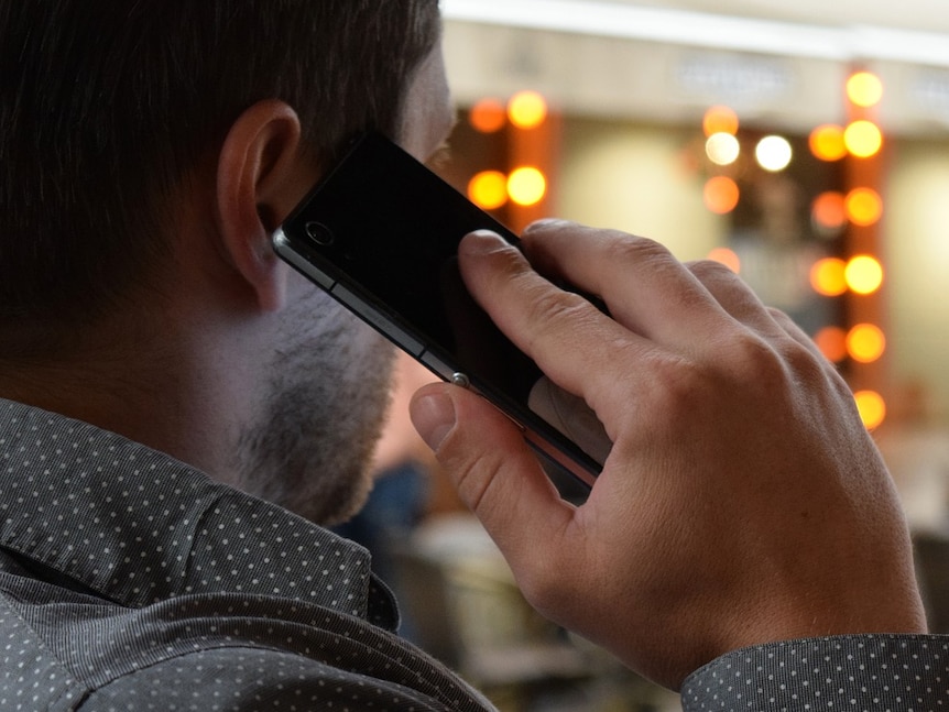 A man wearing a grey collared shirt holds a mobile phone to his ear.