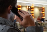 A man wearing a grey collared shirt holds a mobile phone to his ear.