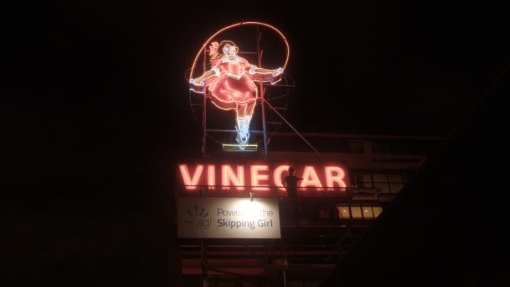 A neon sign in red and white featuring a girl skipping.