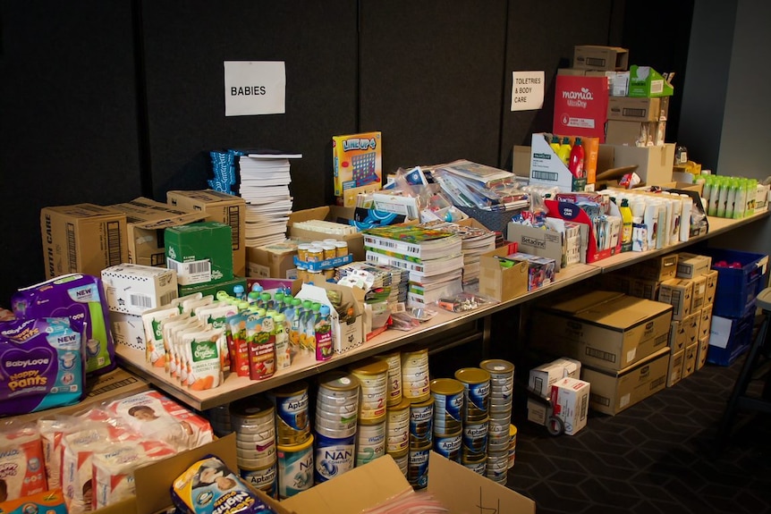 A table with multiple tins of infant milk formula, baby food and nappies.