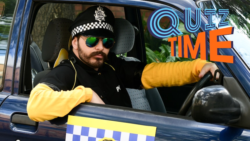 Joe dressed up as a police officer wearing dark shades sitting in a car looking stern.