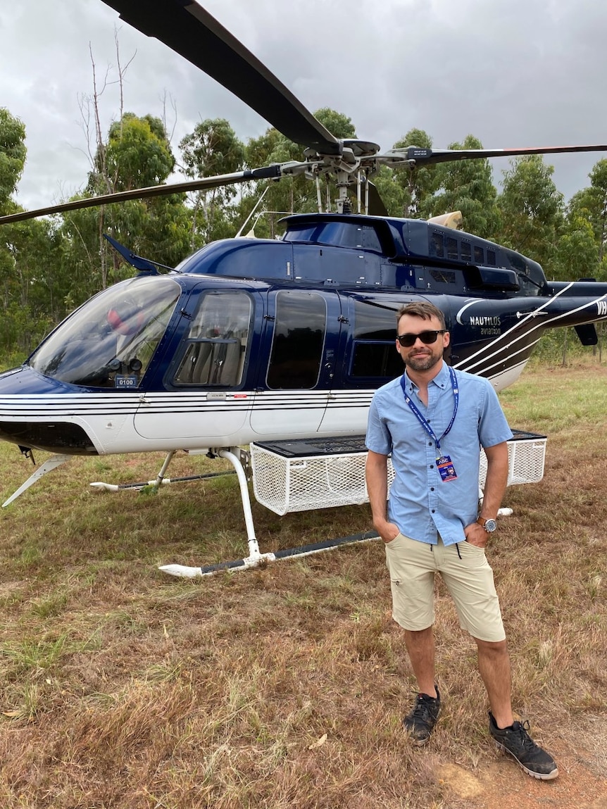 A man stands in front of a helicopter.