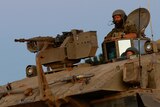A medium shot of the top of an Israeli armoured personnel carrier, with two men in helments poking their heads through the top