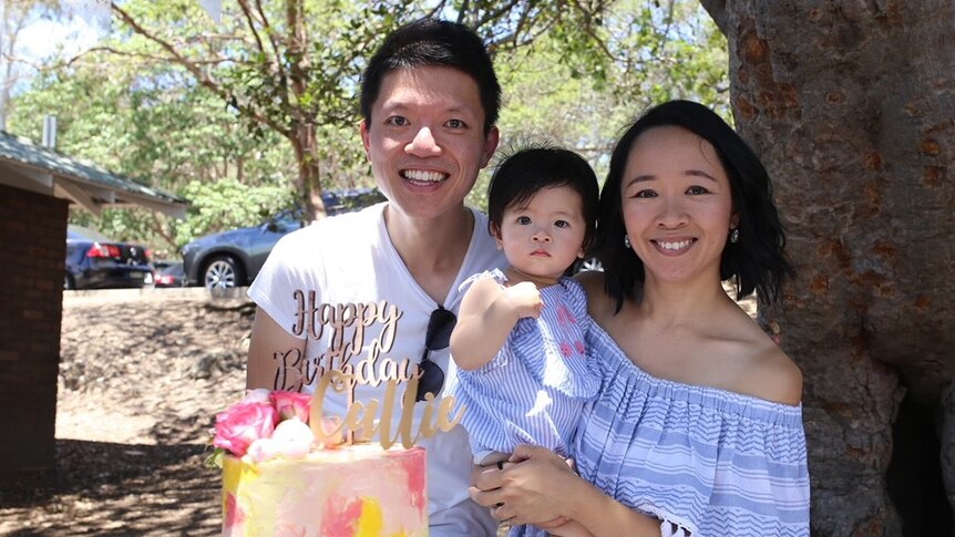 A smiling couple with baby and big cake