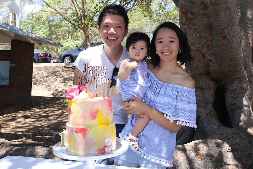 A smiling couple with baby and big cake