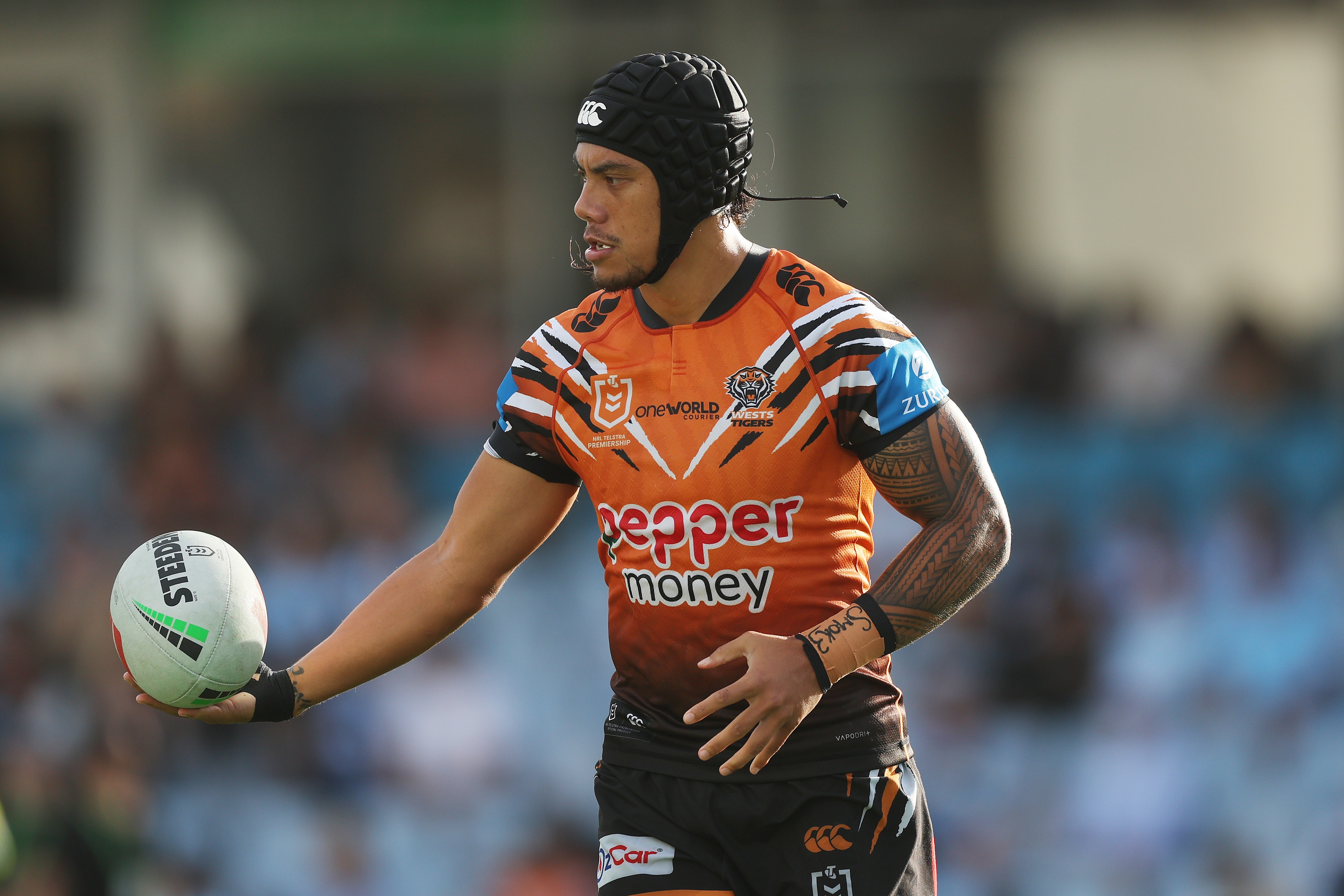 A rugby league player with a head protector on, wearing orange, holds the ball