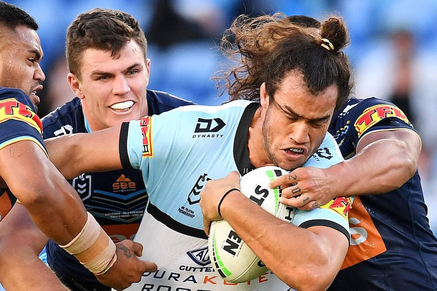 A Cronulla Sharks NRL player holds the ball with his left arm as he is tackled by three Gold Coast Titans players.
