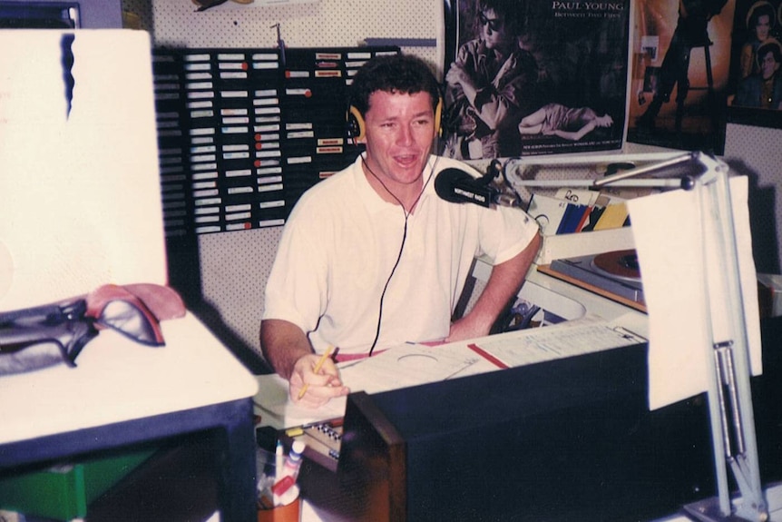 A young man talks in a radio station booth with a big smile on his face