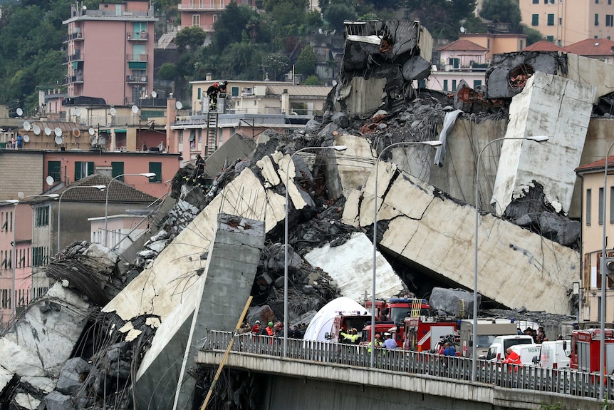 A wide shot shows tons of concrete, wire and rubble collapsed and emergency workers.