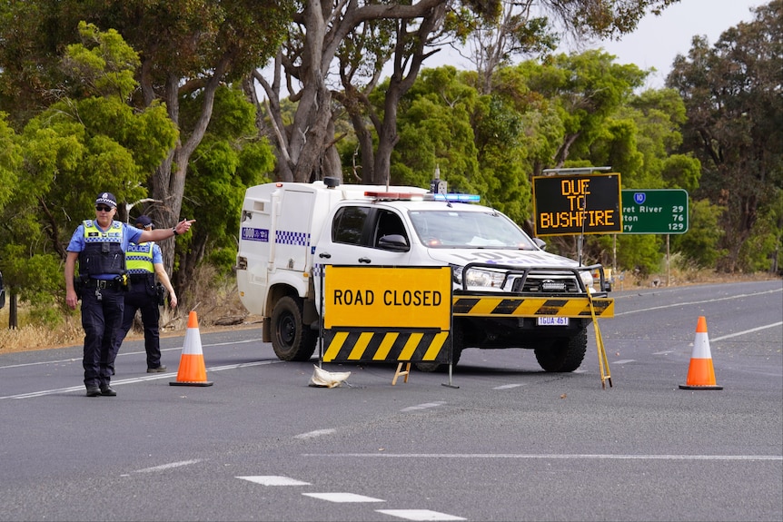 A police car forms a roadblock on Bussell Highway in Karridale with signs and officers alongside the vehicle.