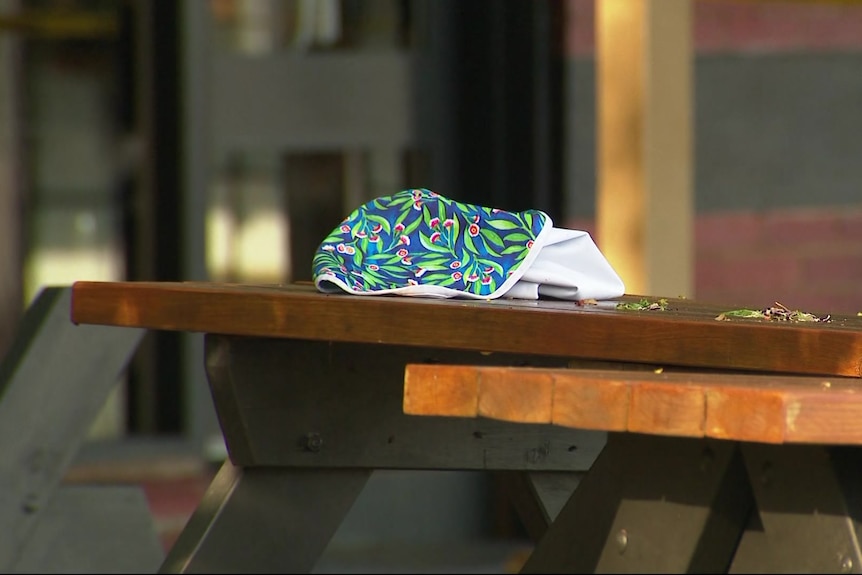 A piece of bright fabric sits on a wooden picnic table, next to a full jug.