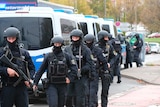 Armed police in protective gear line up with guns out next to a number of police vans
