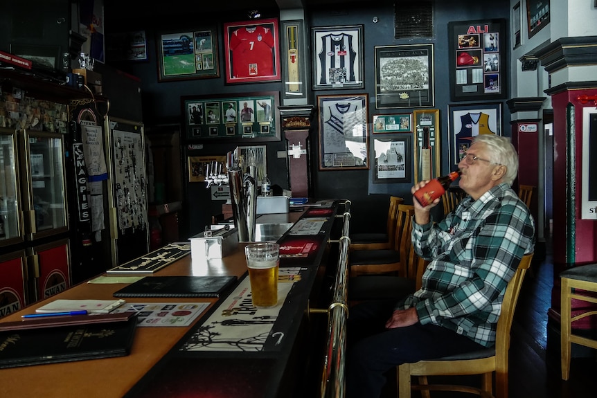 A man drinks a beer in a pub with no lights on