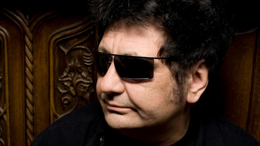 A close up photo of a man in a dark shirt and dark sunglasses