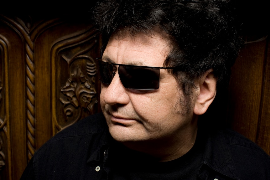 A close up photo of a man in a dark shirt and dark sunglasses