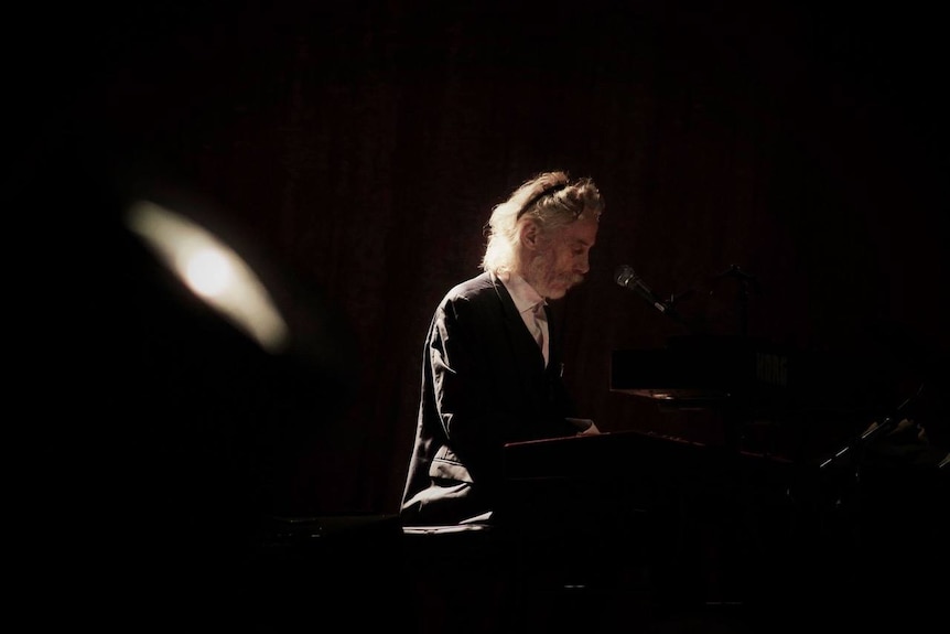 Profile of man playing piano on darkened stage