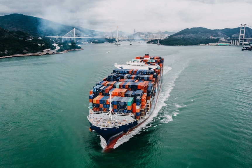 An aerial view of a cargo ship with bridges and smoke in the background.