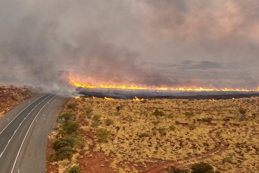 A fire rips through a rural landscape near a highway