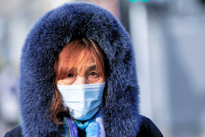 A woman in a face mask and a big hooded blue fur coat