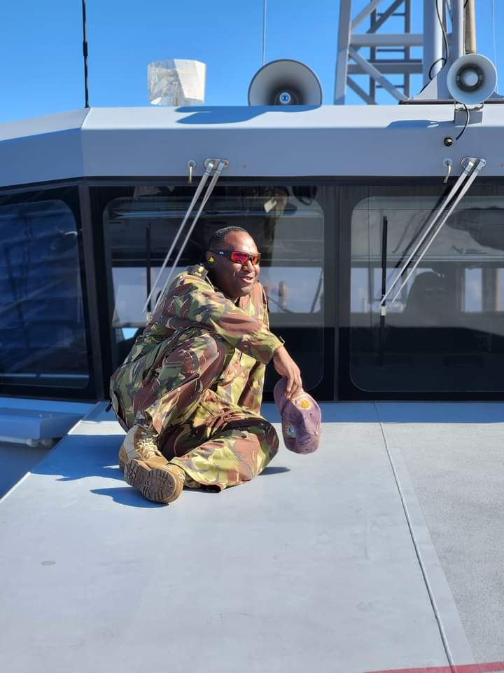PNG man Eric Gwale wearing military fatigue sitting on a boat wearing sunglasses