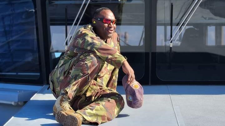 PNG man Eric Gwale wearing military fatigue sitting on a boat wearing sunglasses