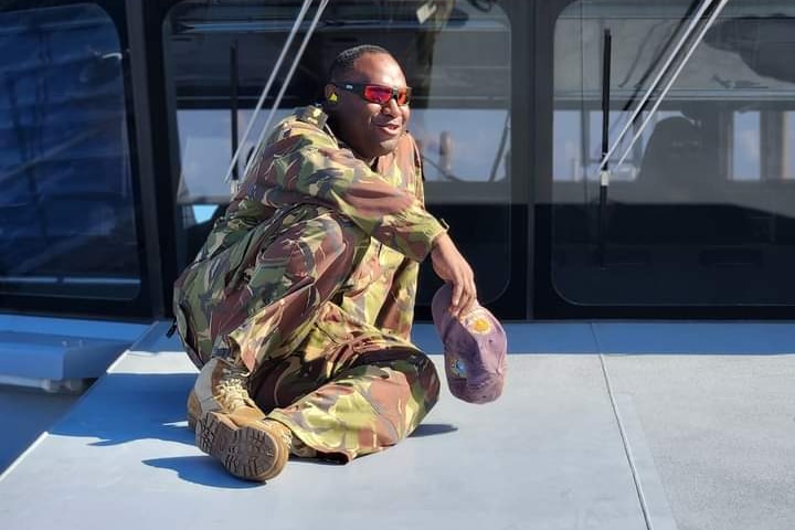 PNG man Eric Gwale wearing military fatigue sitting on a boat wearing sunglasses
