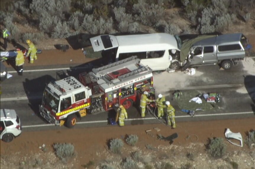 Two vehicles that appear to have collided head-on sit on the side of a road, with a fire truck, ambulance and emergency crews.