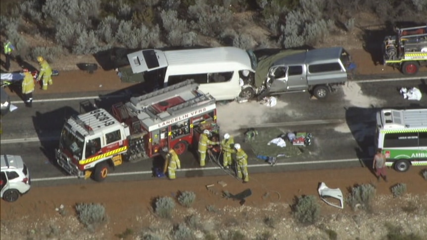 Two vehicles that appear to have collided head-on sit on the side of a road, with a fire truck, ambulance and emergency crews.