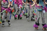 The legs of four females who are all wearing black and white patterned tights and rollerblades on their feet.