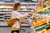 A woman wearing a face mask chooses fruit while grocery shopping with a hand basket