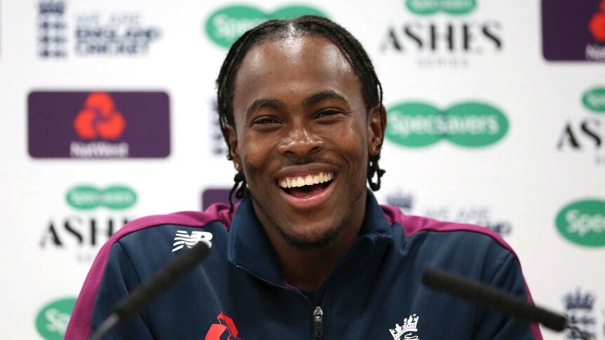 Jofra Archer, wearing an England team tracksuit, smiles and laughs at an Ashes press conference.