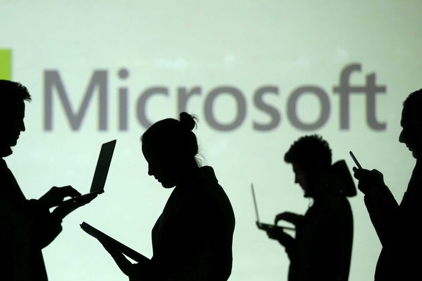 Des silhouettes d'utilisateurs d'ordinateurs portables et d'appareils mobiles sont visibles à côté d'une projection d'écran du logo Microsoft