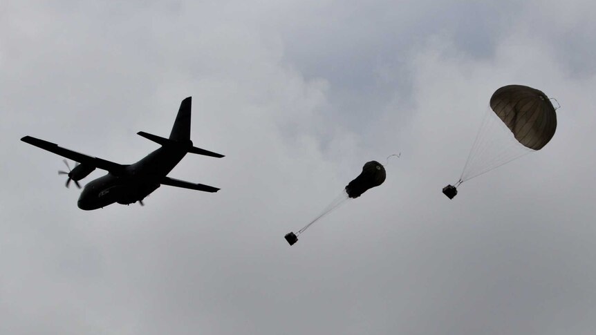 Silhouette of military plane dropping two parcels with parachutes from the sky