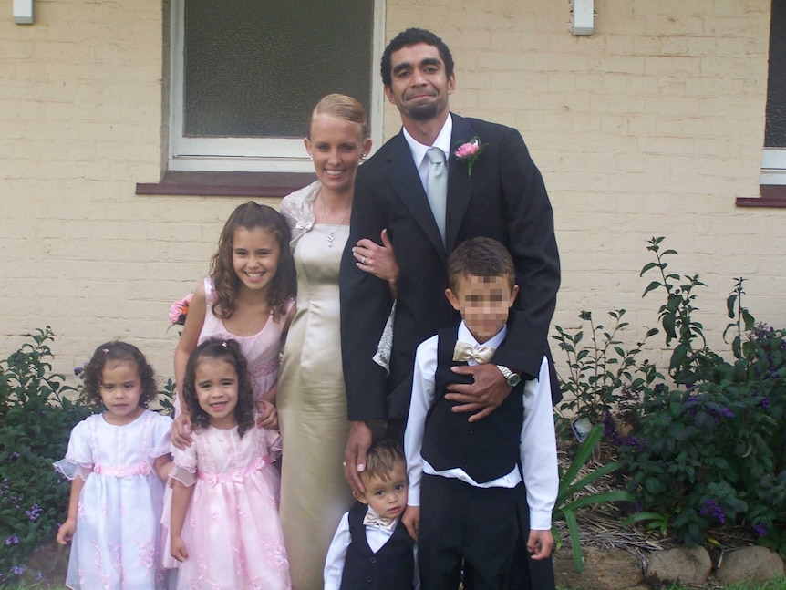 Daniel wears a suit with a pink flower in the lapel, with a woman in a formal dress, and three little girls, arms around a boy.