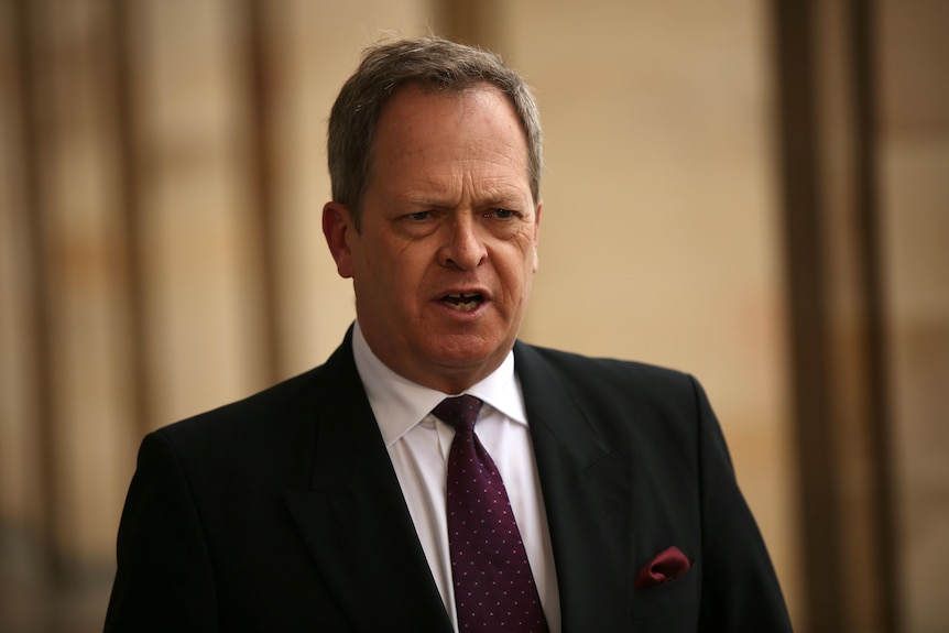 A man in a black suit speaks at a press conference