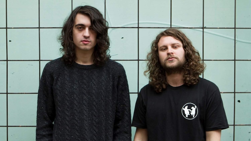 Otologic wearing black tshirts in front of a aqua tiled wall