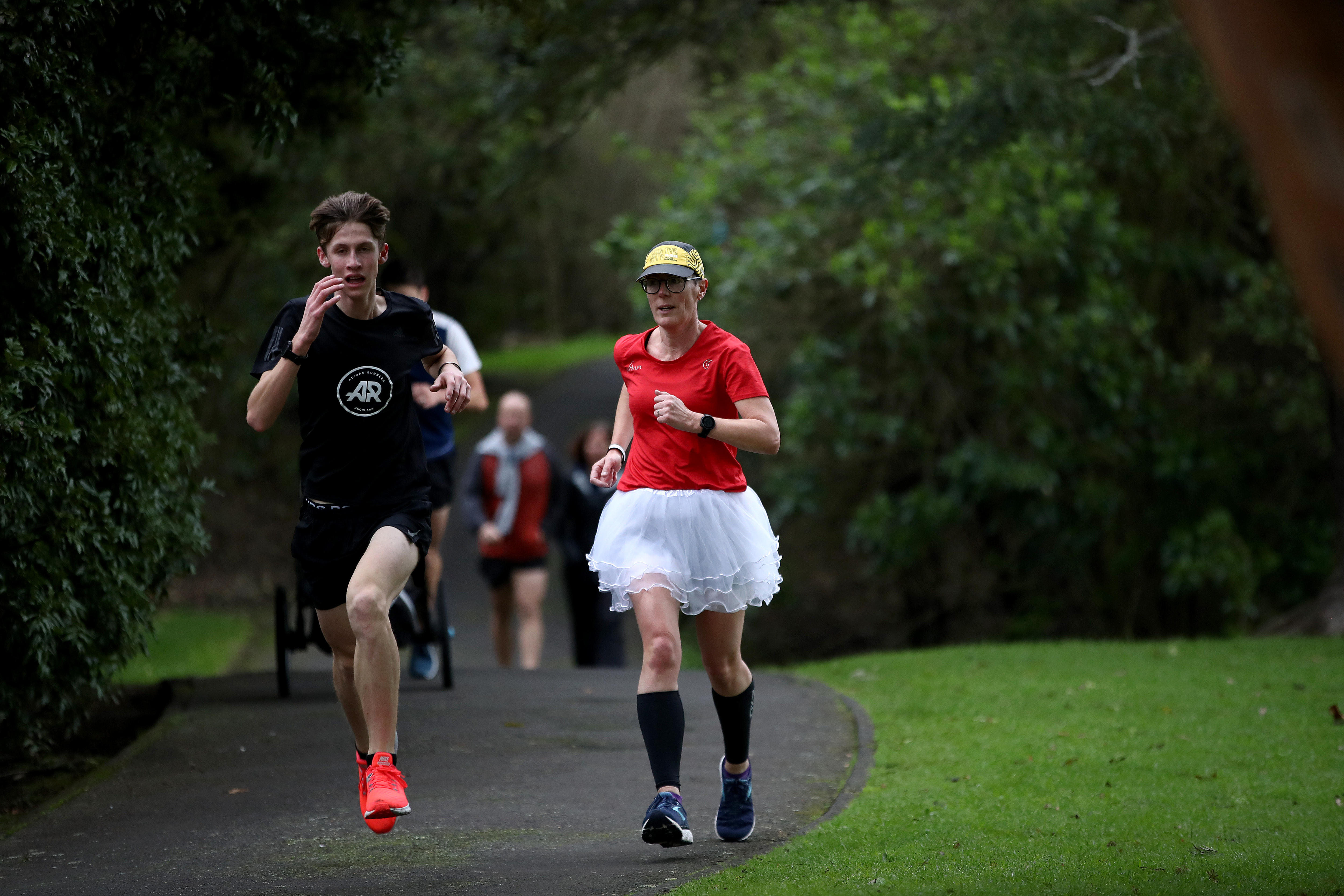 Two parkrunners run, one in a back top the other in a red top and a tutu skirt.