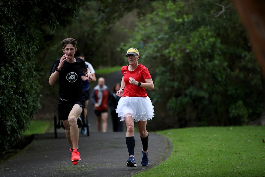 Two parkrunners run, one in a back top the other in a red top and a tutu skirt.