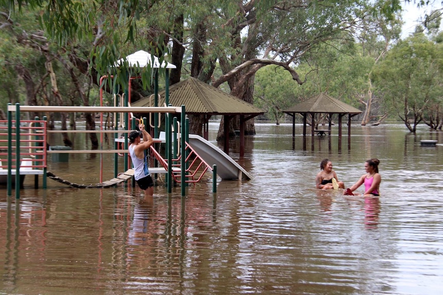 Three people play on playground equipment that is under water.