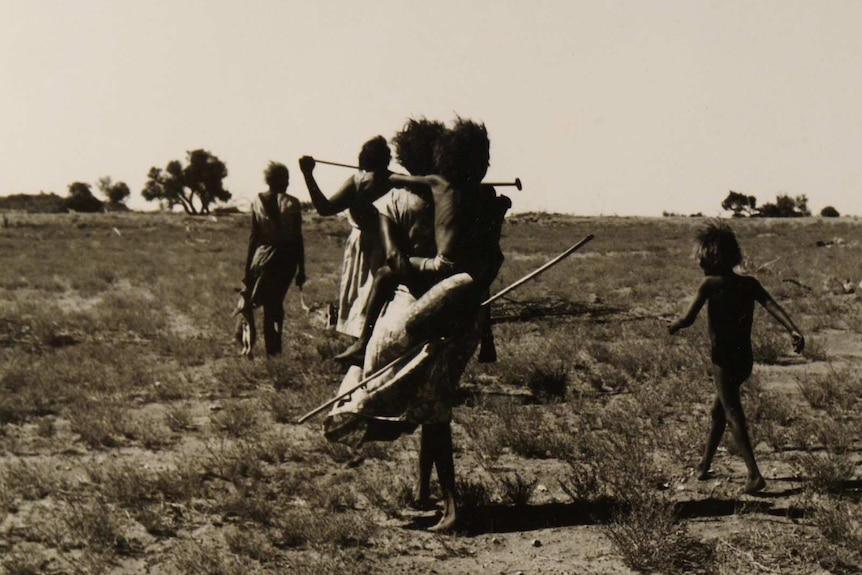A group of woman and children walking away from the camera in a central Australian desert landscape