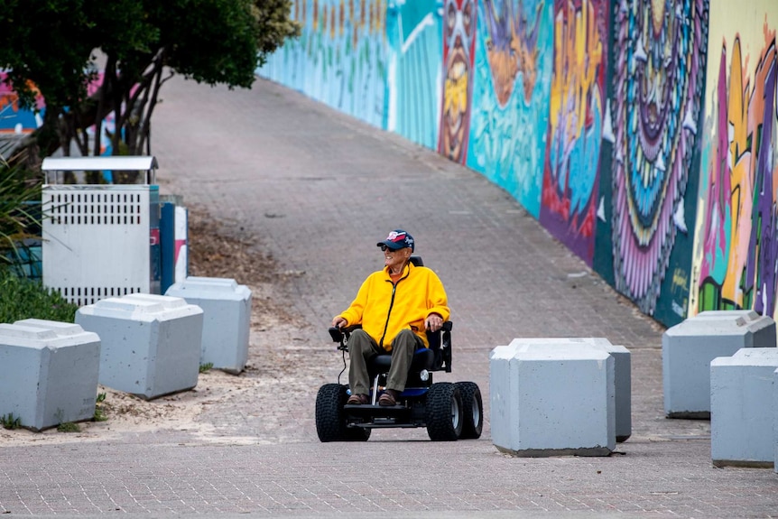 A man with a bright yellow top wheels down the street in a motorised wheelchair.