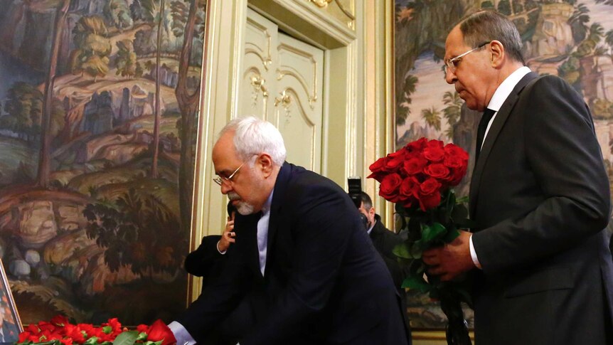 Sergei Lavrov (R) and his Iranian counterpart Mohammad Javad Zarif lay flowers in front of photo of Andrei Karlov.