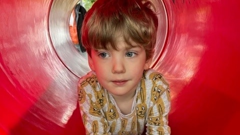 A boy in a red play tunnel. 