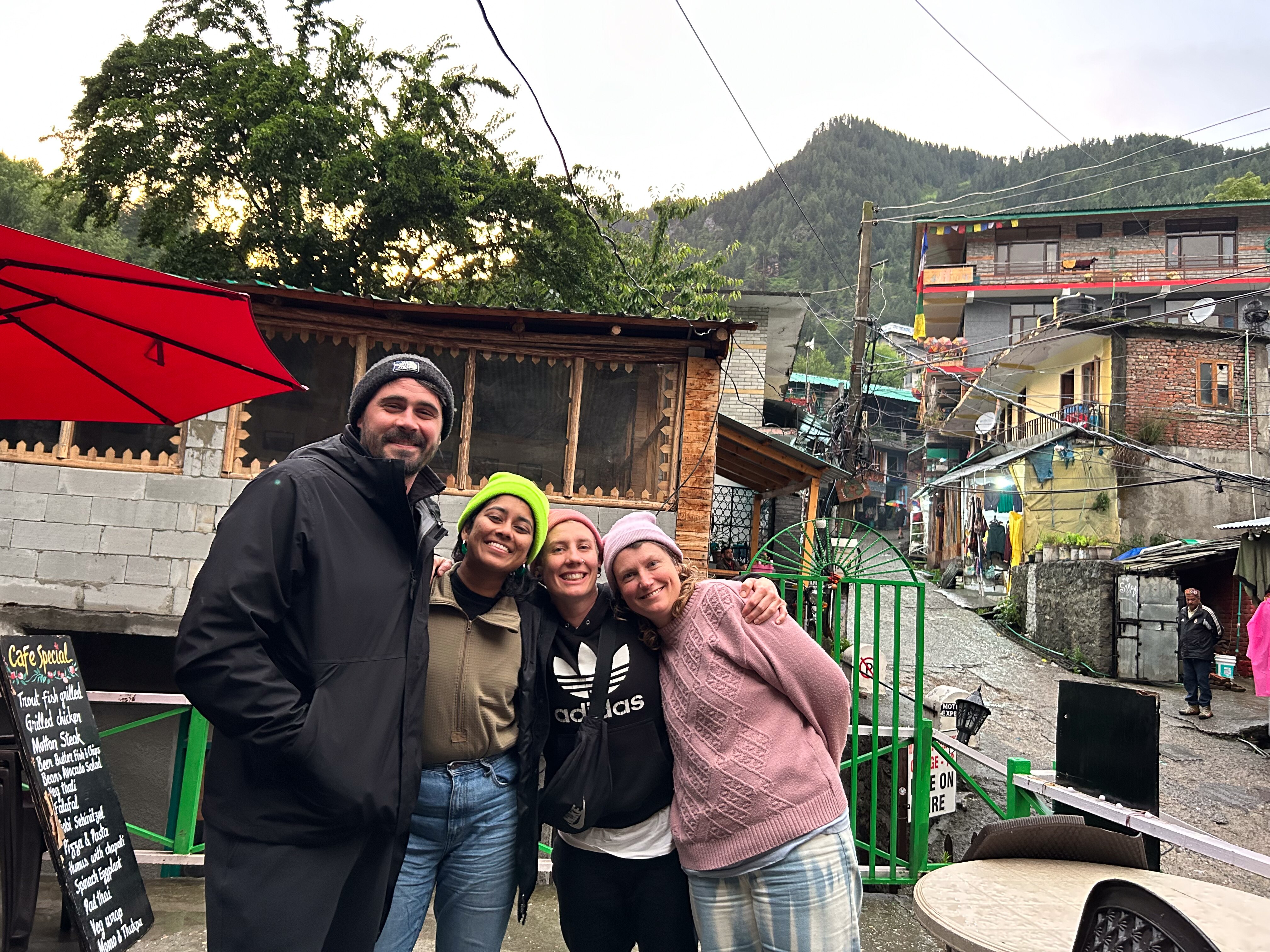 Four young people wearing beanies and jumpers gather together smiling in an open courtyard next to cobbled street